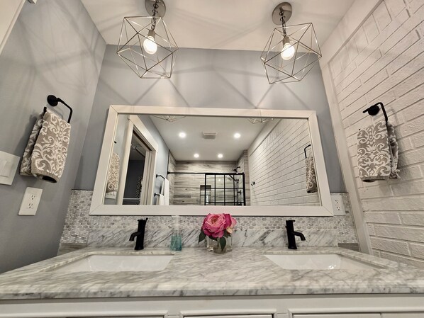 A bathroom with a large mirror, two sinks, and a shower area.