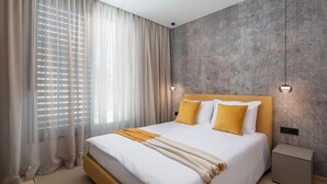 Un dormitorio moderno con una cama grande, cortinas translúcidas, un pared con textura y una mesita de noche.