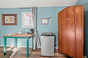 Une pièce avec un meuble en bois, une petite table sur laquelle se trouve une machine à café, une carte encadrée et une fenêtre avec des rideaux.
