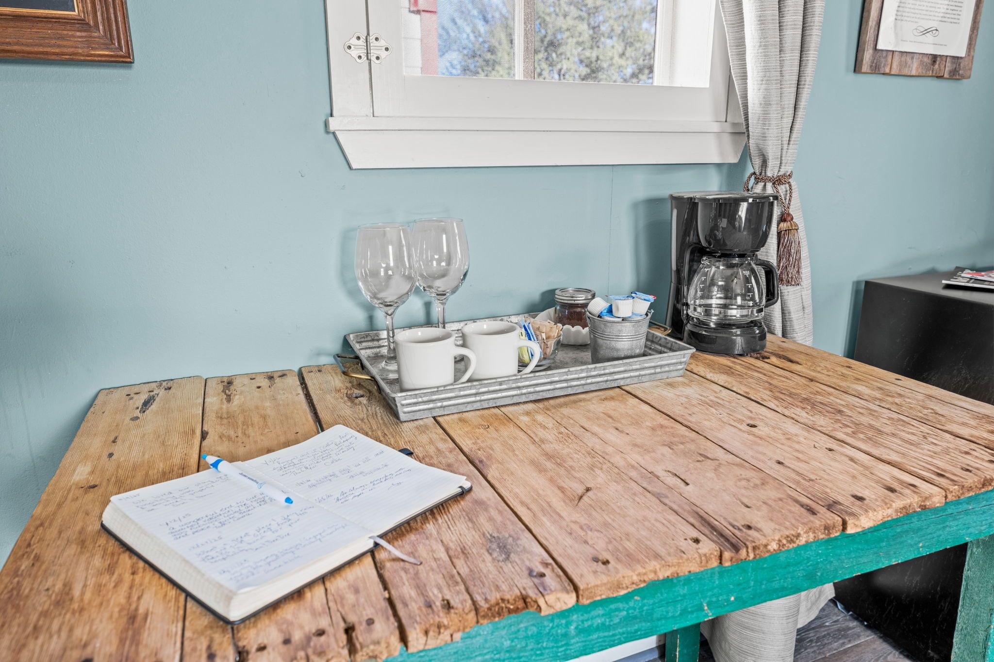 A wooden table with a notebook, a tray with mugs, glasses, and a coffee maker.