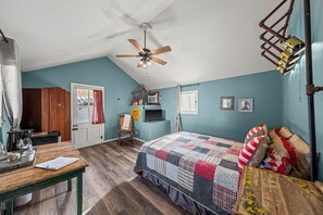 A bedroom with a bed, a desk, a chair, a ceiling fan, and a window.