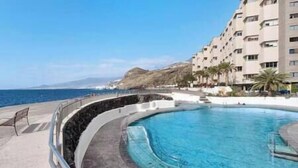 A swimming pool with a curved design, surrounded by a stone wall and a metal railing. - VV Miramar Sunset Tabaiba (Tabaiba)