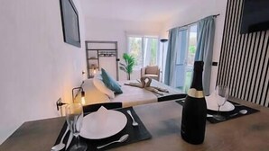 A modern dining area with a table set for two, a bottle of champagne, and a view of the living room and balcony. - BIMBA Studio Park (La Quinta)