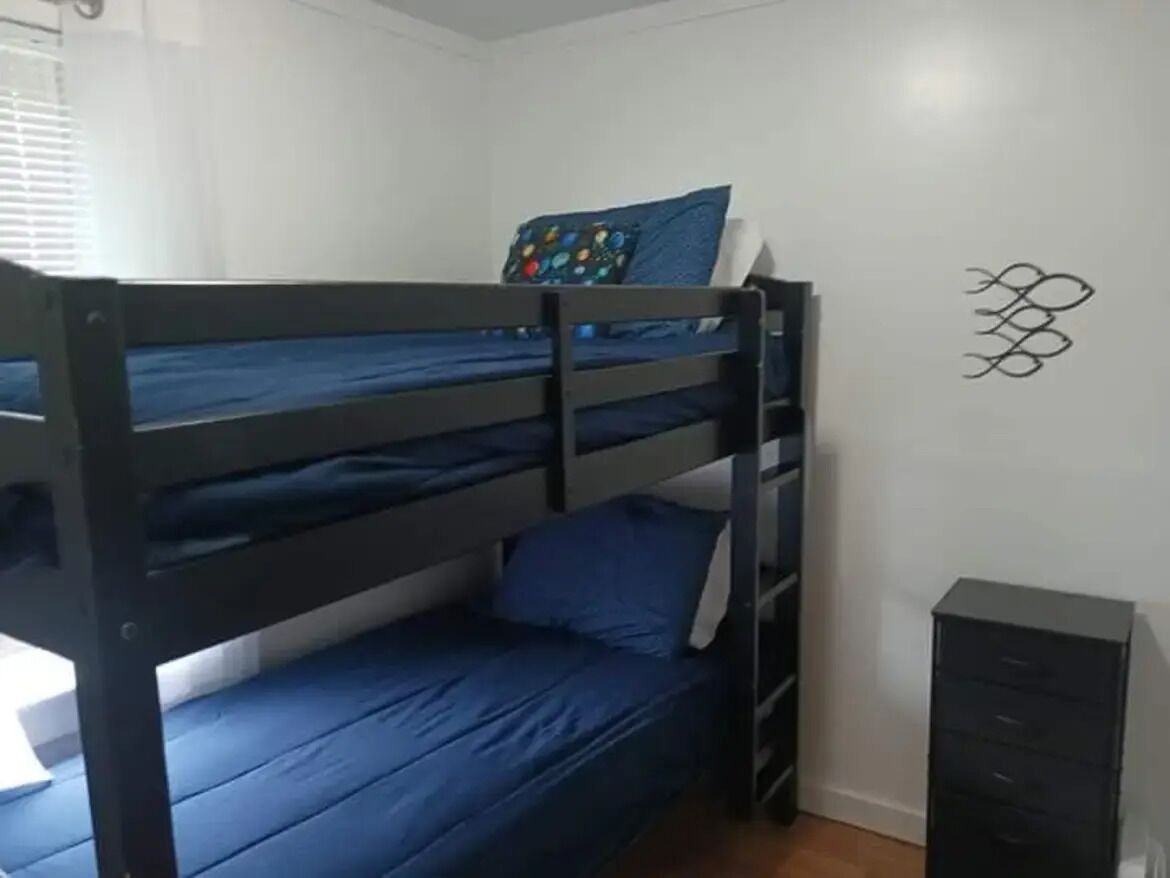 Ein Etagenbett mit blauer Bettwäsche, ein kleines Schränkchen und ein Wandbild.