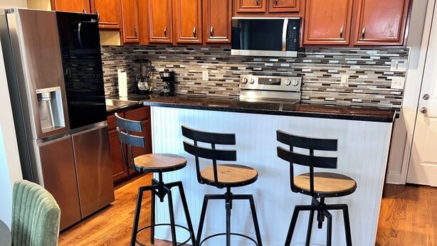 A modern kitchen with wooden cabinets, stainless steel appliances, and a central island with bar stools. - ATL Modern Retreat: 3BR, 8 Guests, Near Downtown & Airport (Atlanta)