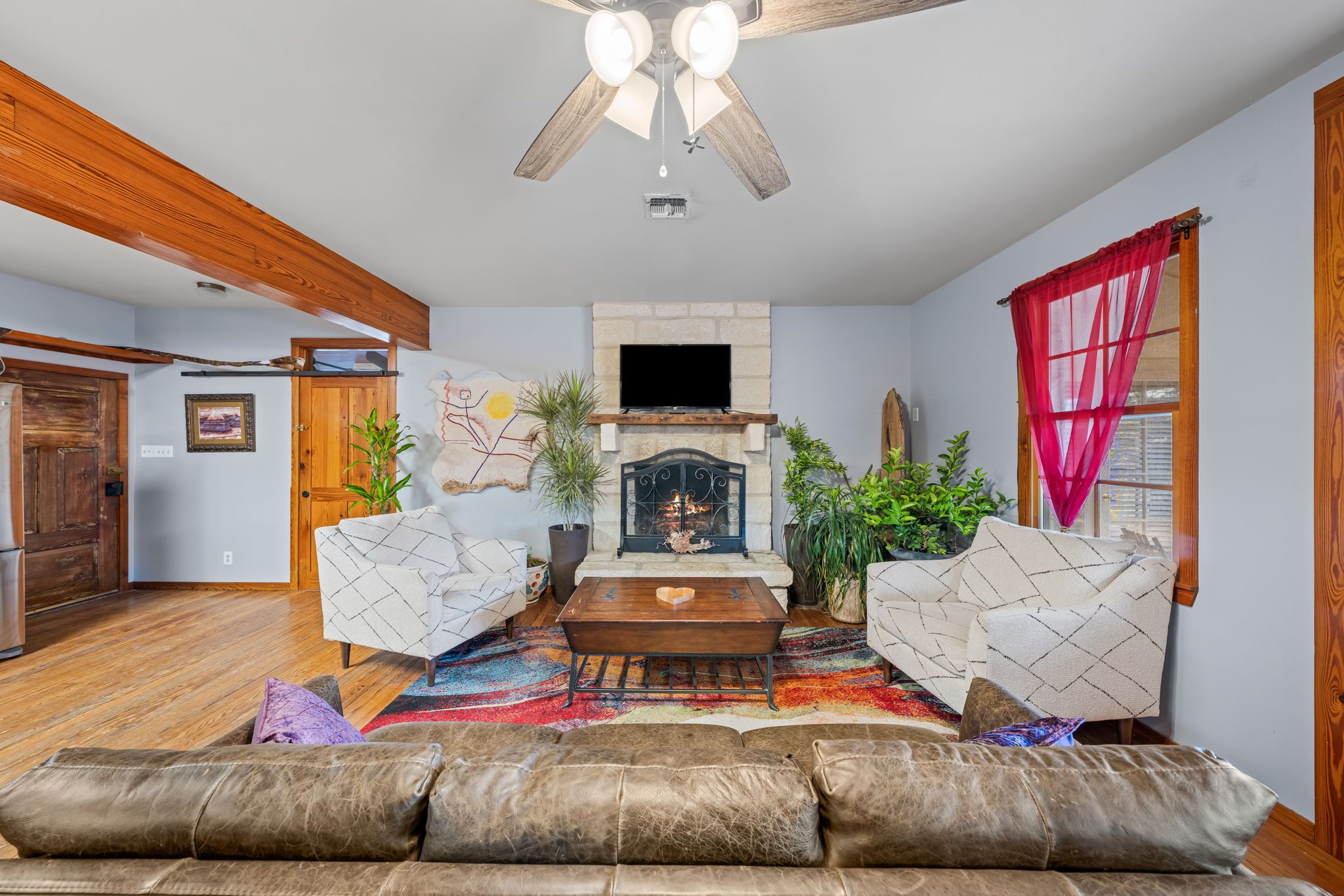 A living room with a fireplace, two armchairs, a sofa, and a ceiling fan.