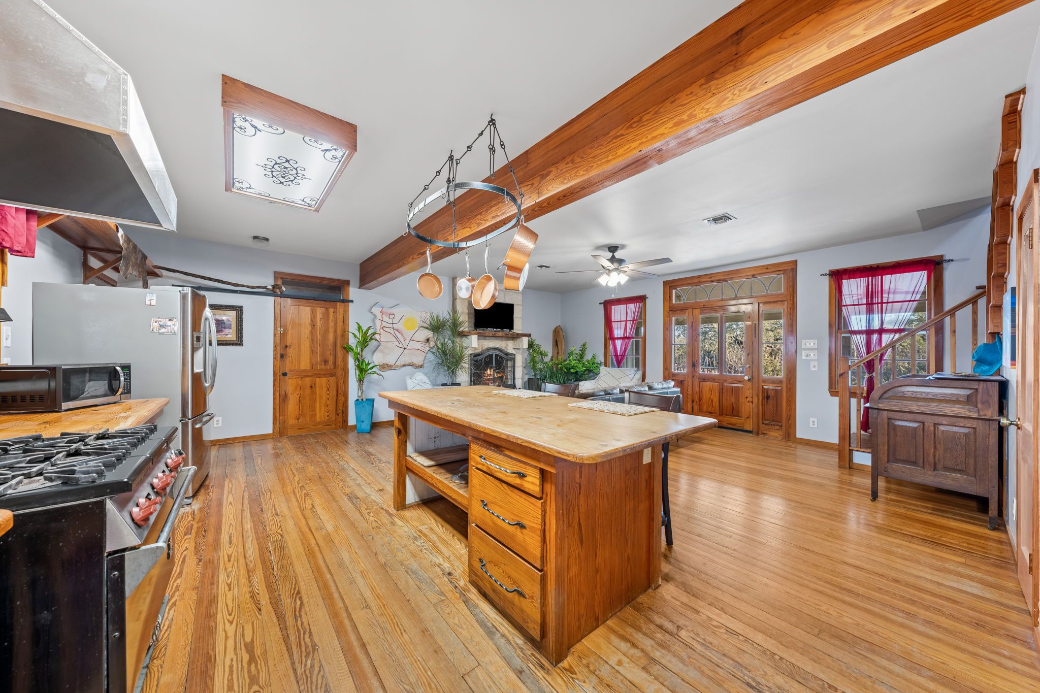 A spacious kitchen with wooden flooring, a central island, and a stone fireplace.