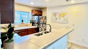 A modern kitchen with a central island, wooden cabinets, a refrigerator covered in magnets, a window with blinds, and a world map on the wall. - Private Entrance\Modern&Cozy Central Bliss\King Villa\55" 4k Roku\Full Kitchen (Colorado Springs)