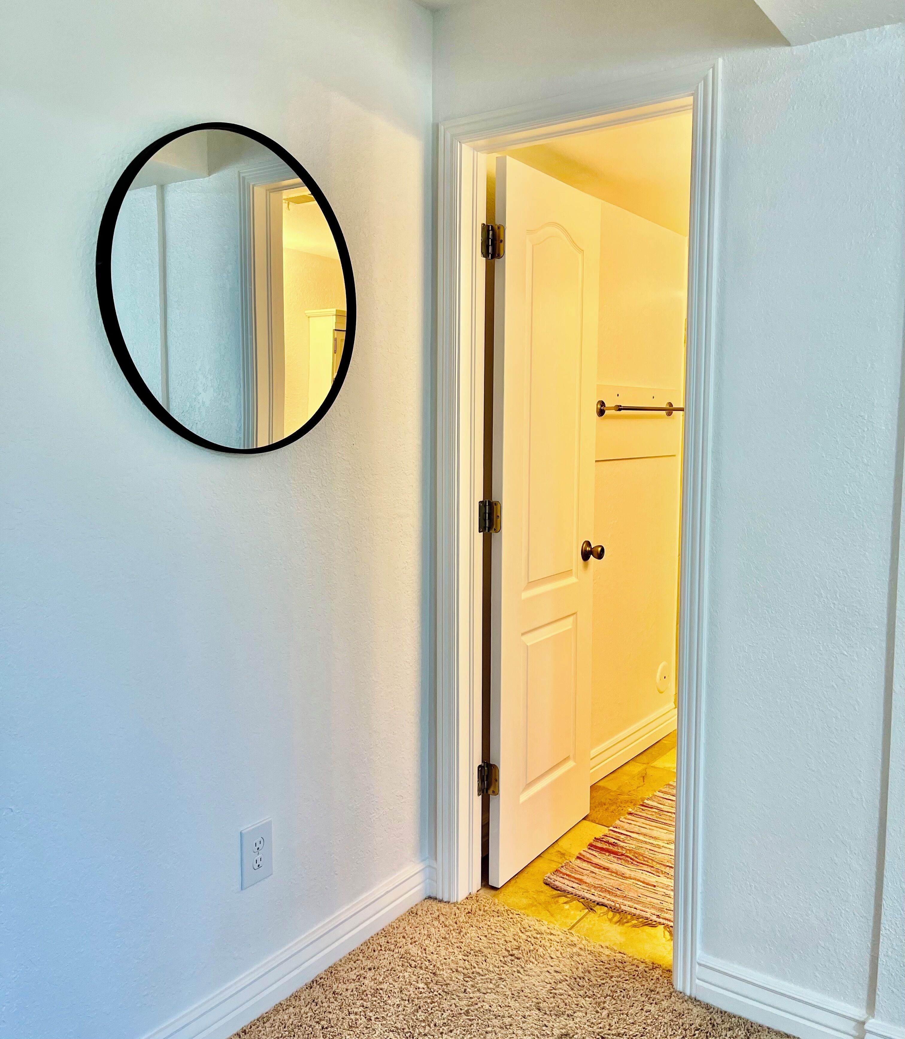 A hallway with a white door, a round mirror on the wall, and a carpeted floor.