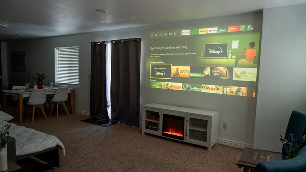 A cozy room with a large wall-mounted TV displaying a Disney+ interface, a fireplace, a dining area, and a bed. - Private Entrance\Modern&Cozy Central Bliss\King Villa\55" 4k Roku\Full Kitchen (Colorado Springs)
