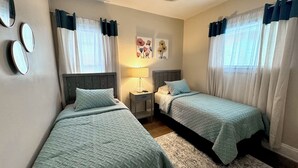 A bedroom with two beds, a nightstand, a lamp, and artwork on the wall. - Farmhouse In The City CLE Clinic-Long Stays Welcome - 2bd/1bth WiFi, Full Kitch (Shaker Heights)