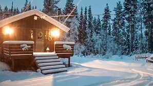 Une cabane en bois dotée d’un porche à l’avant, entourée d’arbres couverts de neige.