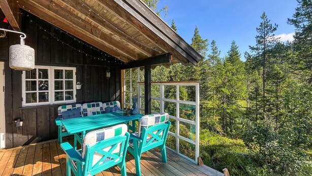 Une terrasse en bois avec une table et des chaises, une fenêtre donnant sur les arbres et un luminaire suspendu.