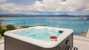 Un jacuzzi con dos copas de vino blanco y un cuenco de fresas, con vistas a un cuerpo de agua y montañas al fondo.
