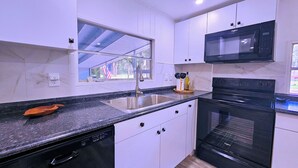 A modern kitchen with white cabinets, a black countertop, a stainless steel sink, a microwave, and an oven. - MANATEE MANOR, Swim with Manatees! 3bdrm 2 bth home Crystal River with PET Bdrm! (Crystal River)