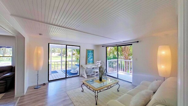 A spacious living room with a white couch, a glass coffee table, and a view of a patio with outdoor furniture. - MANATEE MANOR, Swim with Manatees! 3bdrm 2 bth home Crystal River with PET Bdrm! (Crystal River)