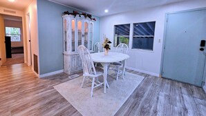 A dining area with a white table and chairs, a decorative cabinet, and a window with blinds. - MANATEE MANOR, Swim with Manatees! 3bdrm 2 bth home Crystal River with PET Bdrm! (Crystal River)