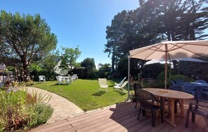 Eine Holzterrasse mit Tisch und Stühlen, umgeben von einer Rasenfläche und Bäumen.