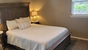 Une chambre avec un grand lit, deux tables de chevet avec des lampes, une chaise et une fenêtre avec des stores.