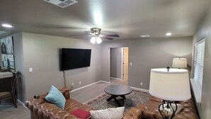 Un salon comprenant un canapé en cuir, un téléviseur à écran plat, un ventilateur de plafond, une lampe et un coin repas avec une table et des chaises.