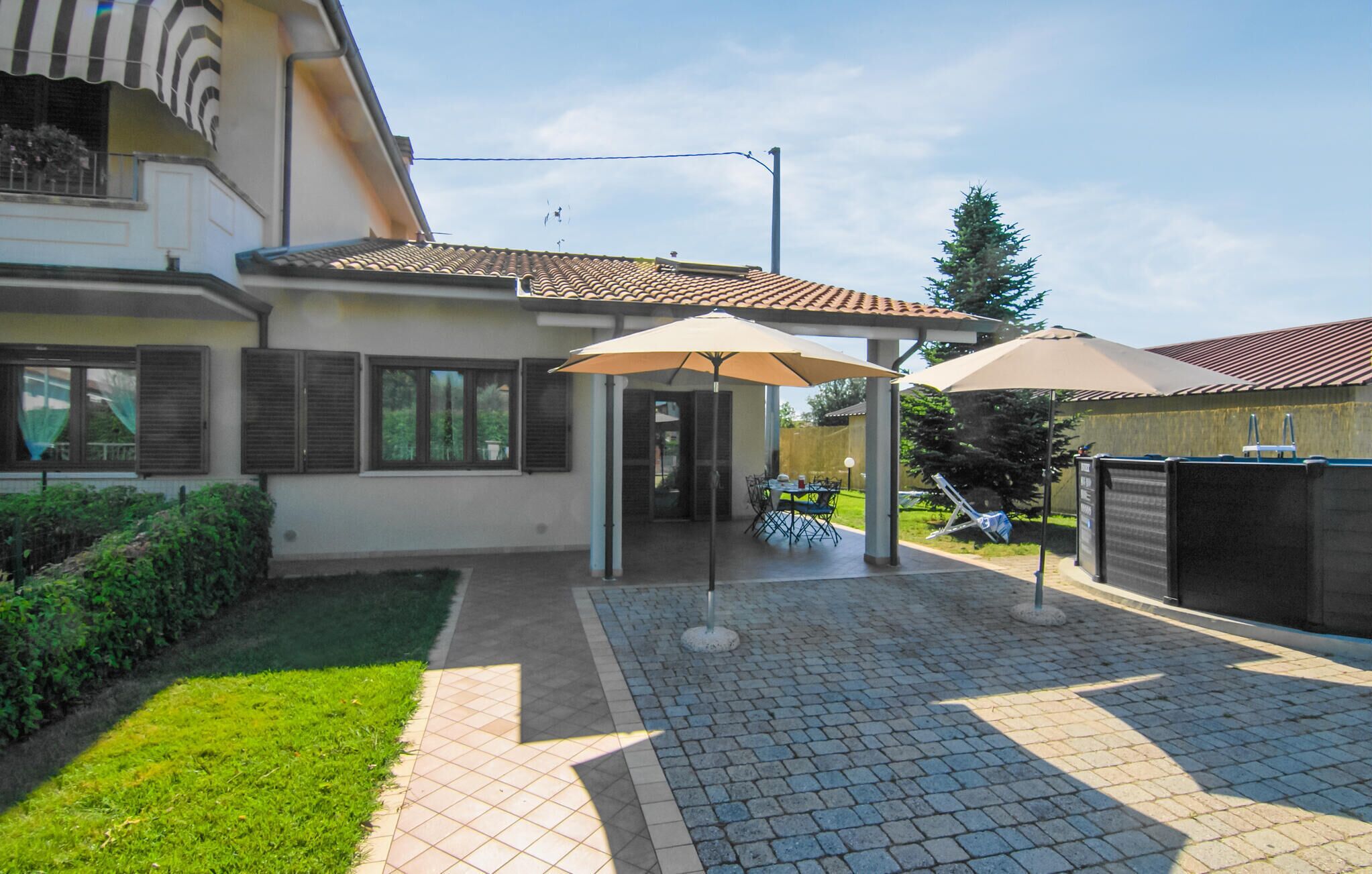 A covered patio area with a table and chairs, a lawn, and a house with a tiled roof.