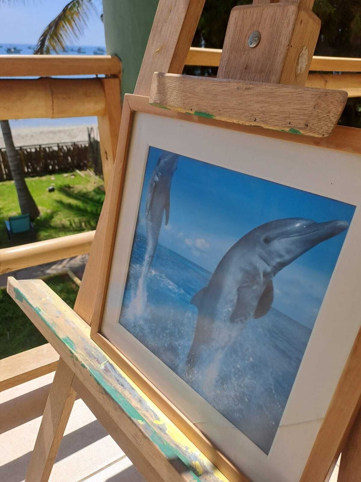 A wooden easel holding a framed picture of dolphins in the ocean.