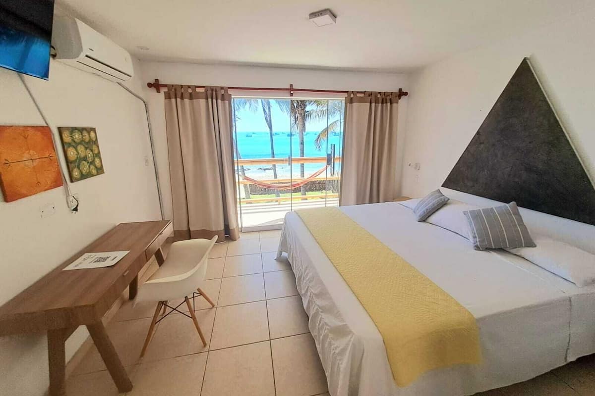 A hotel room with a bed, a desk, a chair, and a view of the beach.