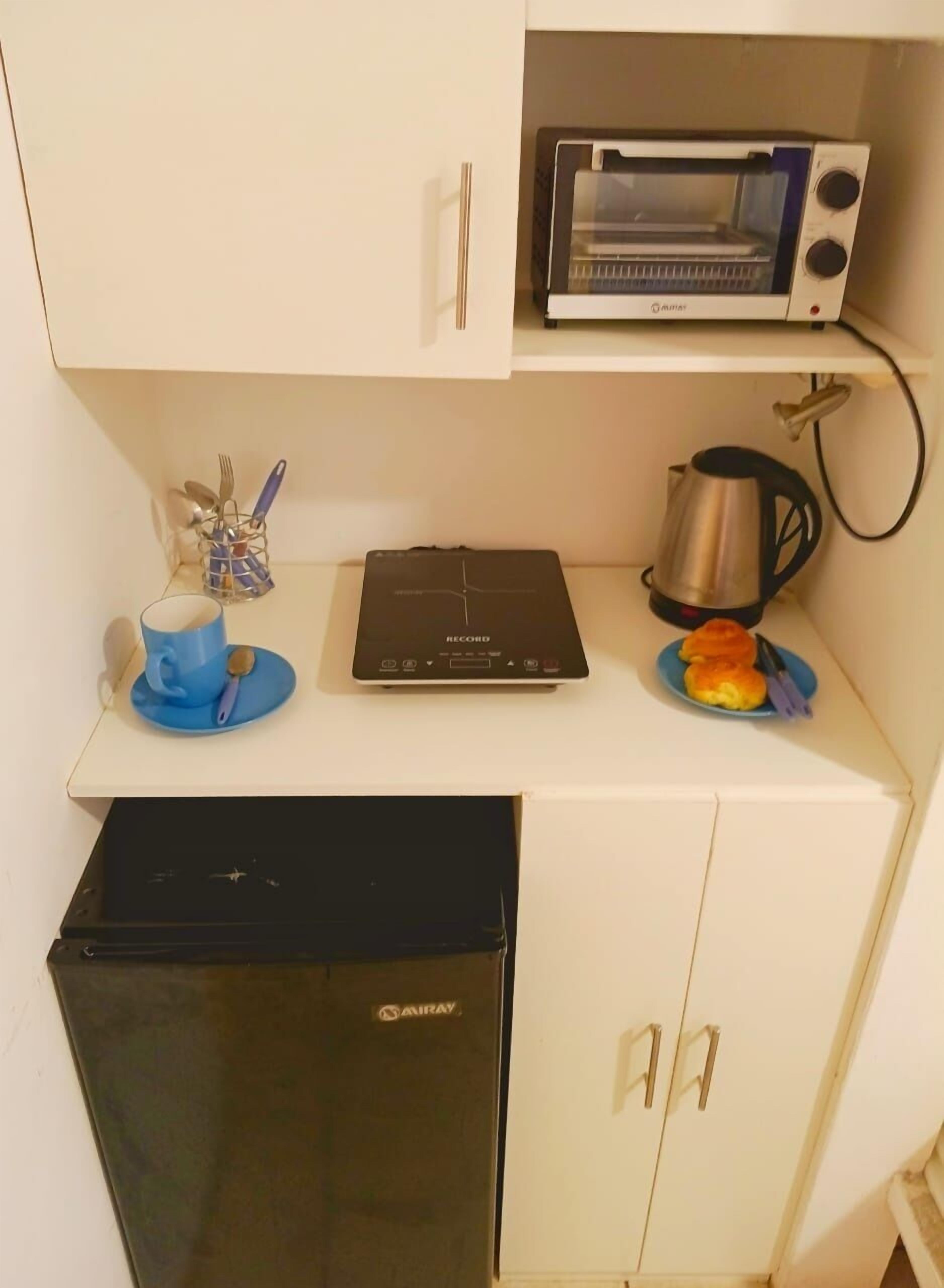 Una kitchenette compacta con un tostador, una tetera, una taza de café y un refrigerador pequeño.