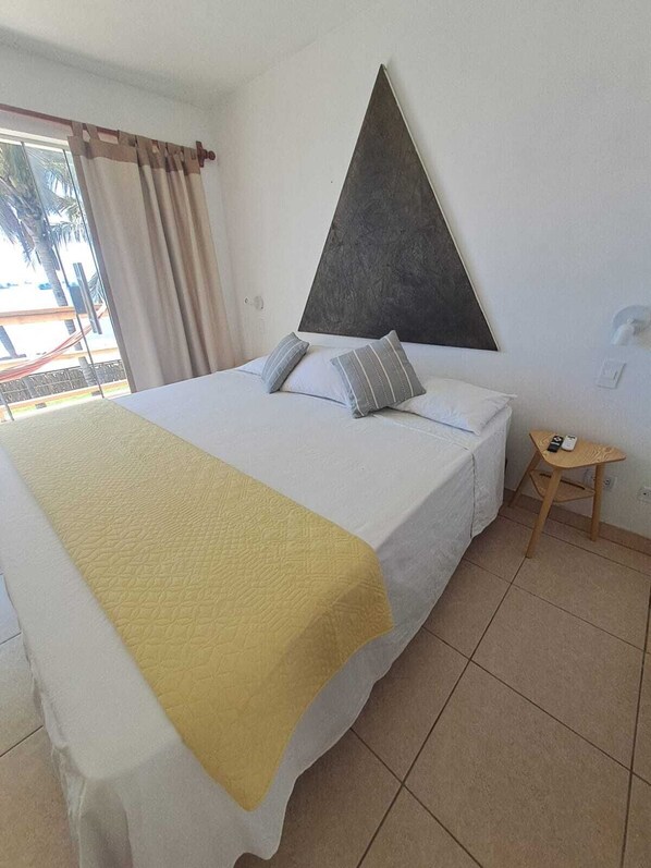 A hotel room with a bed, a small table, and a view of palm trees through the window. - Hotelier Home (Máncora)