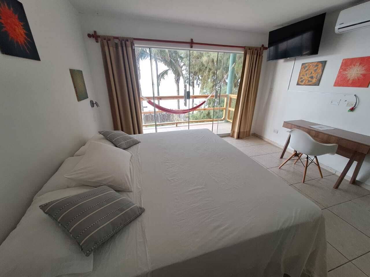 A bedroom with a large bed, a desk, and a TV on the wall.