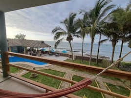 Un balcón con vista al océano, palmeras, una piscina y mobiliario exterior.
