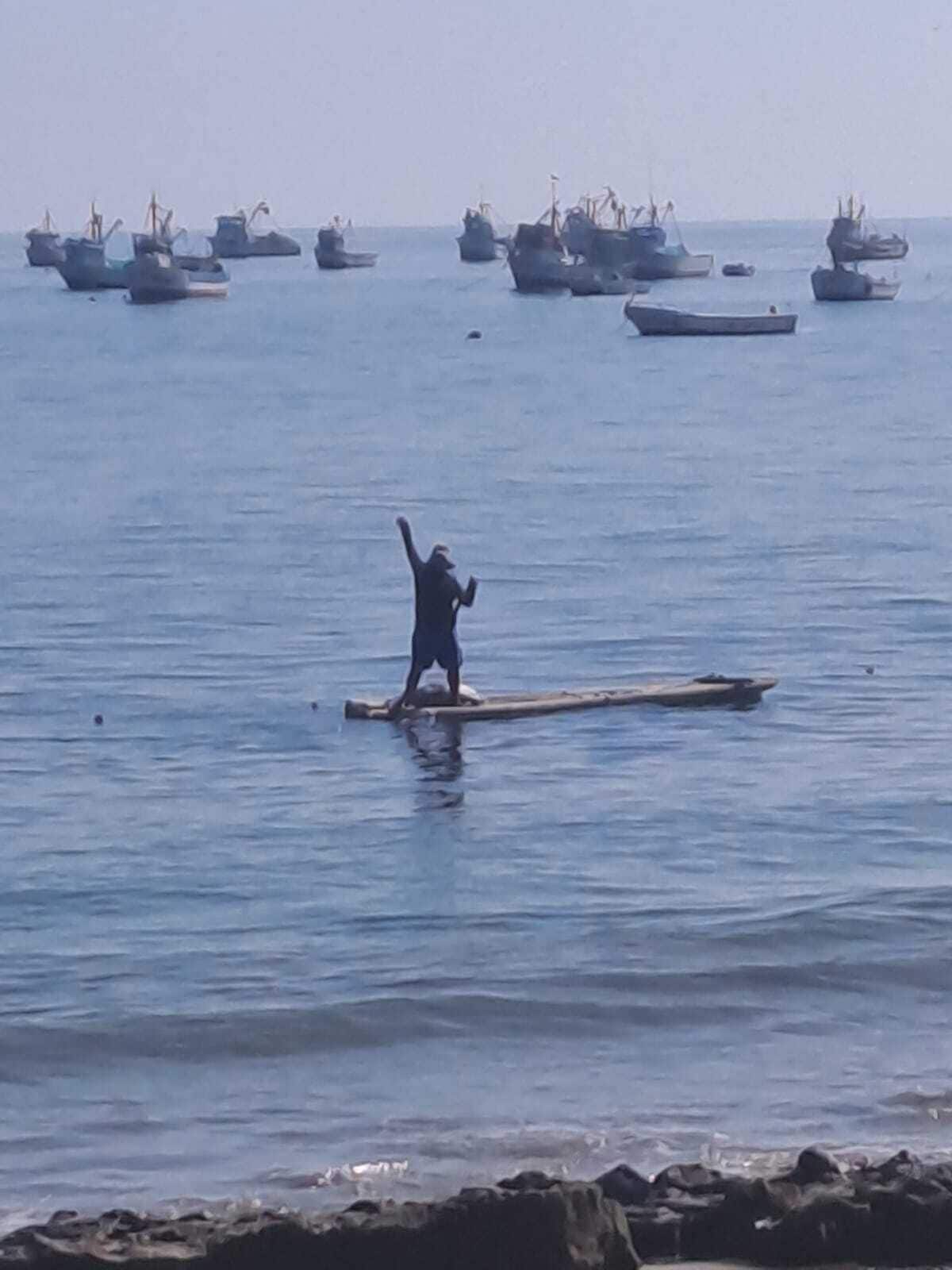 Une personne se tient sur une plateforme flottante, au milieu d’une étendue d’eau, avec plusieurs bateaux en arrière-plan.