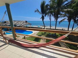 Un balcón con hamaca, piscina y vista al mar.