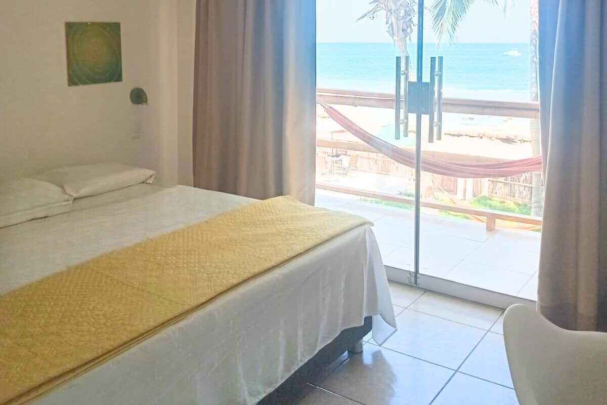 A hotel room with a bed, a view of the beach, and a hammock outside.