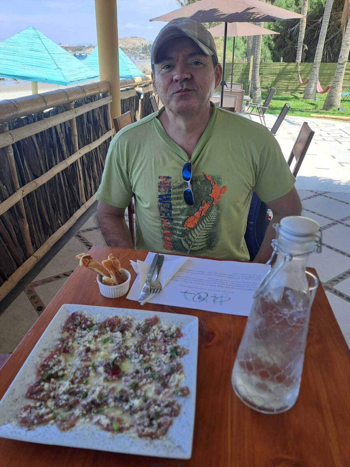 A person seated at an outdoor table with a plate of food, a bottle, and a menu.