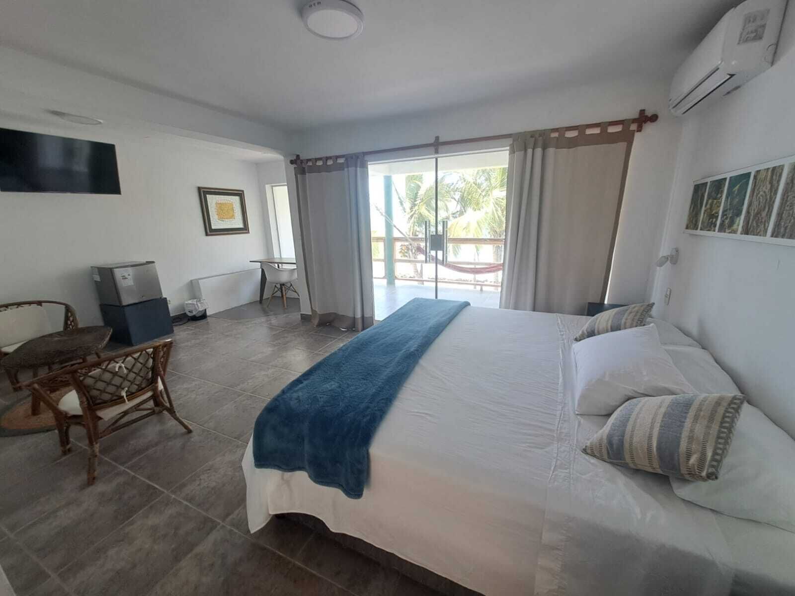 Un dormitorio con una cama grande, un escritorio y una silla. Se ve una ventana con cortinas y vistas a la vegetación.