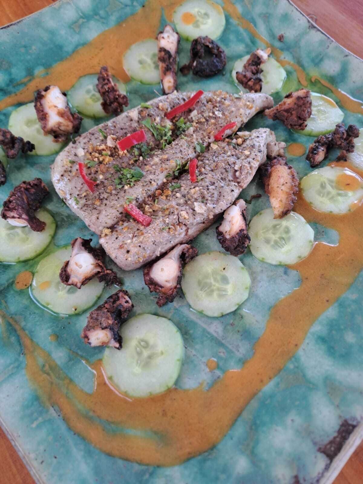 A plate with a fish fillet, cucumber slices, and a sauce.