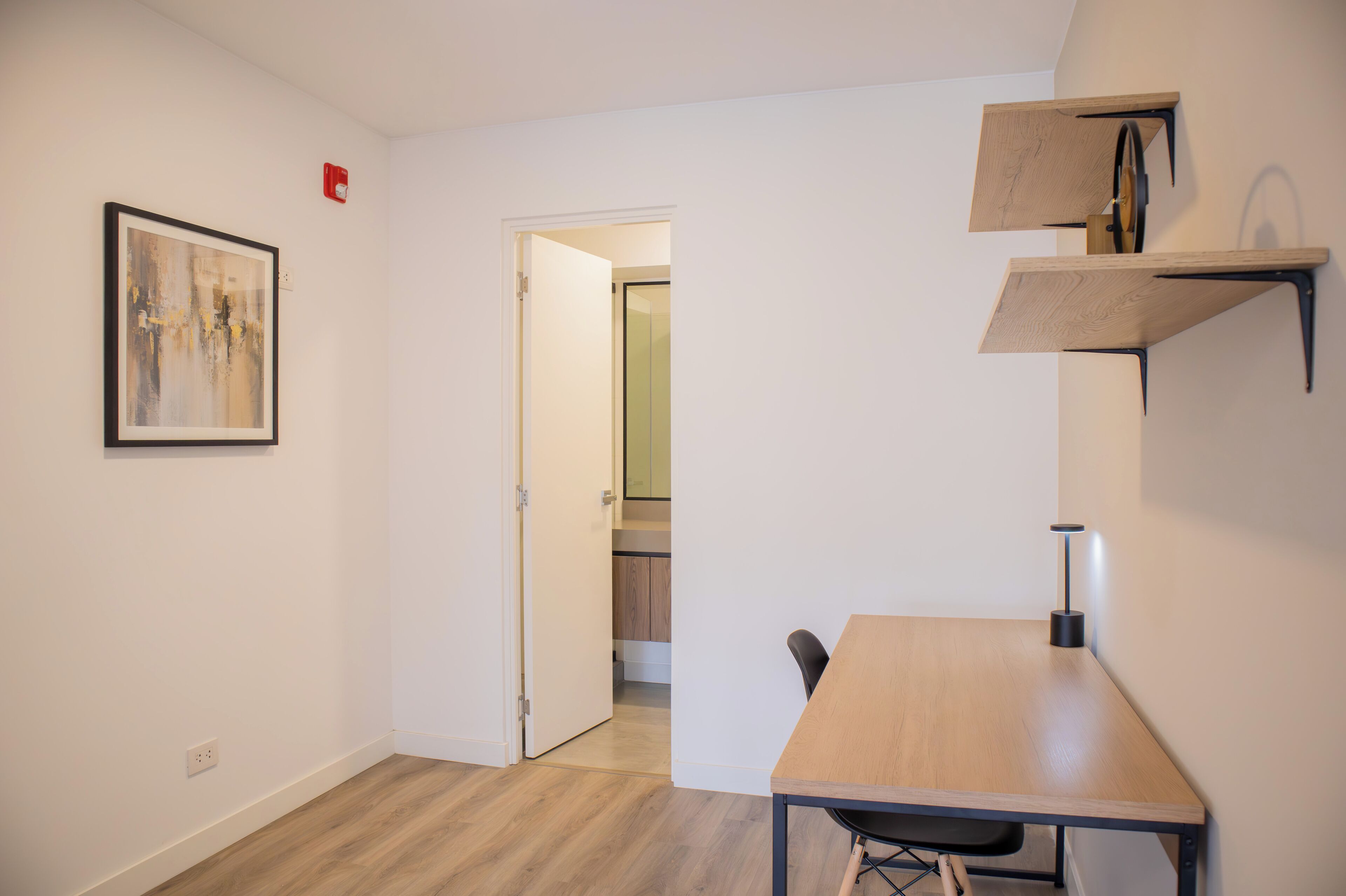 Quarto pequeno e moderno com uma mesa e cadeiras de madeira, um quadro abstrato emoldurado e estantes embutidas.