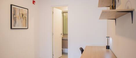 A small, modern room with a wooden table and chairs, a framed abstract painting, and built-in shelves.