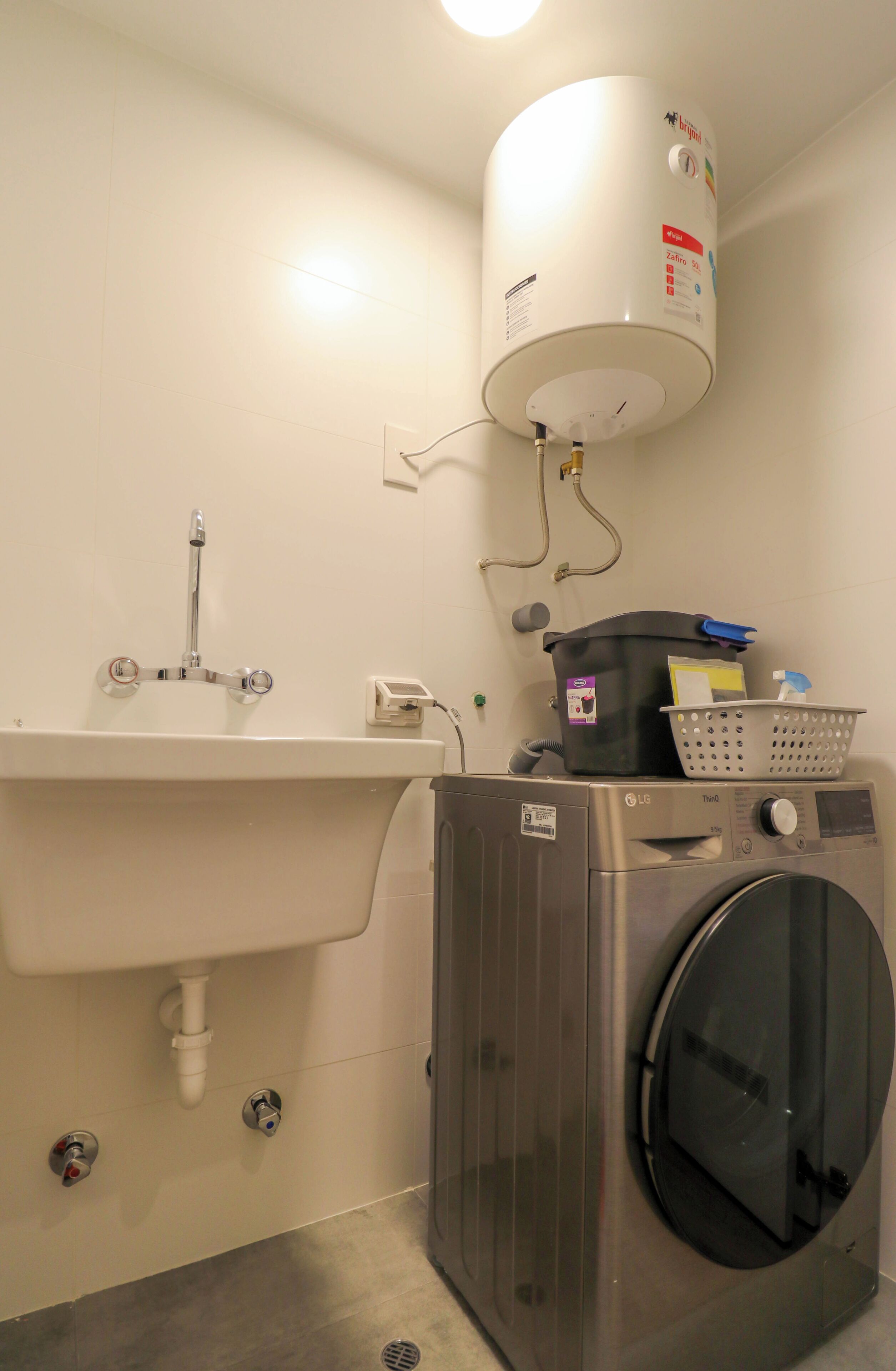 A compact bathroom with a sink, a washing machine, and a water heater.