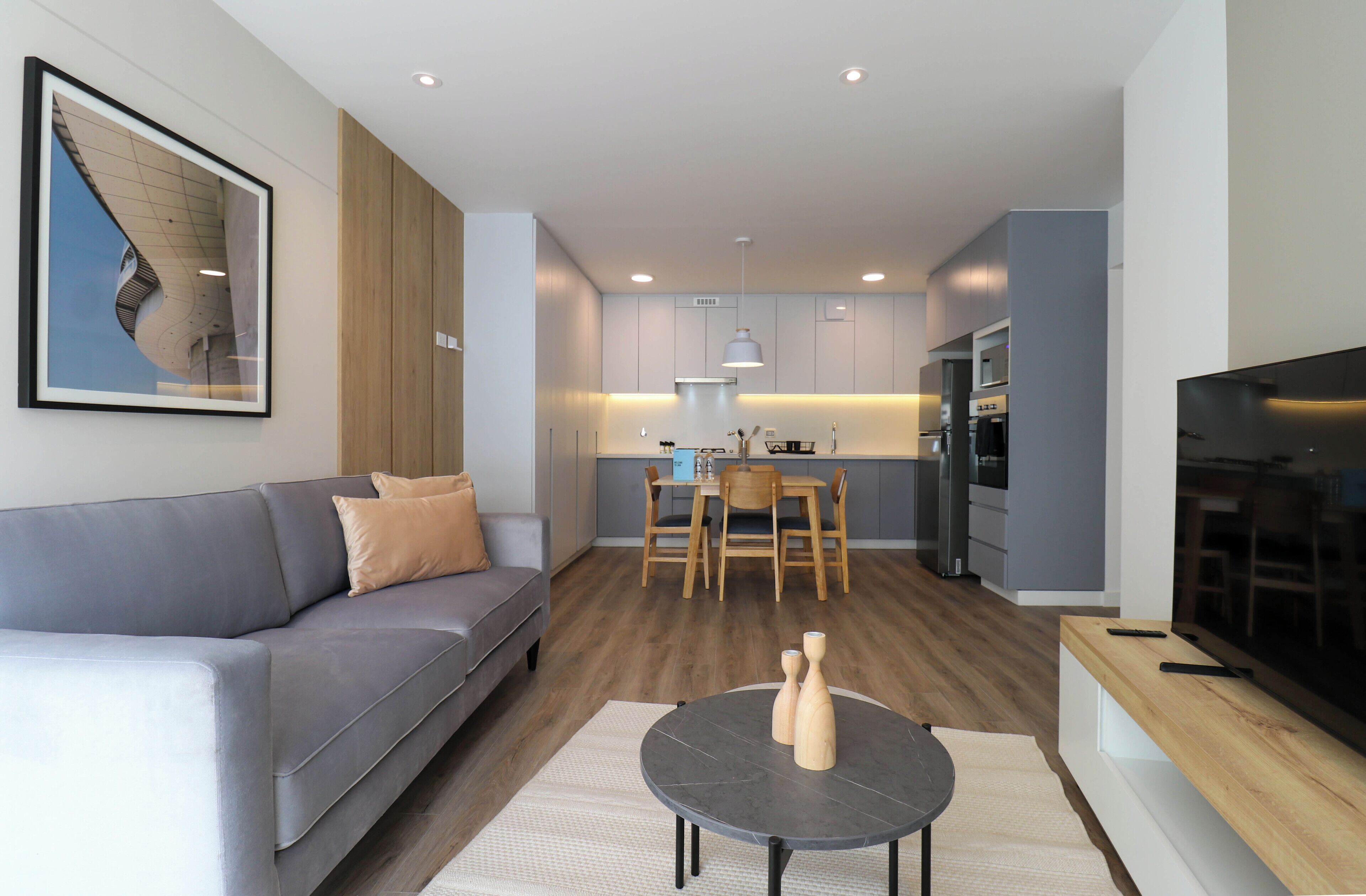 A modern living room with a grey sofa, a round coffee table with candles, and a TV on a wooden stand.