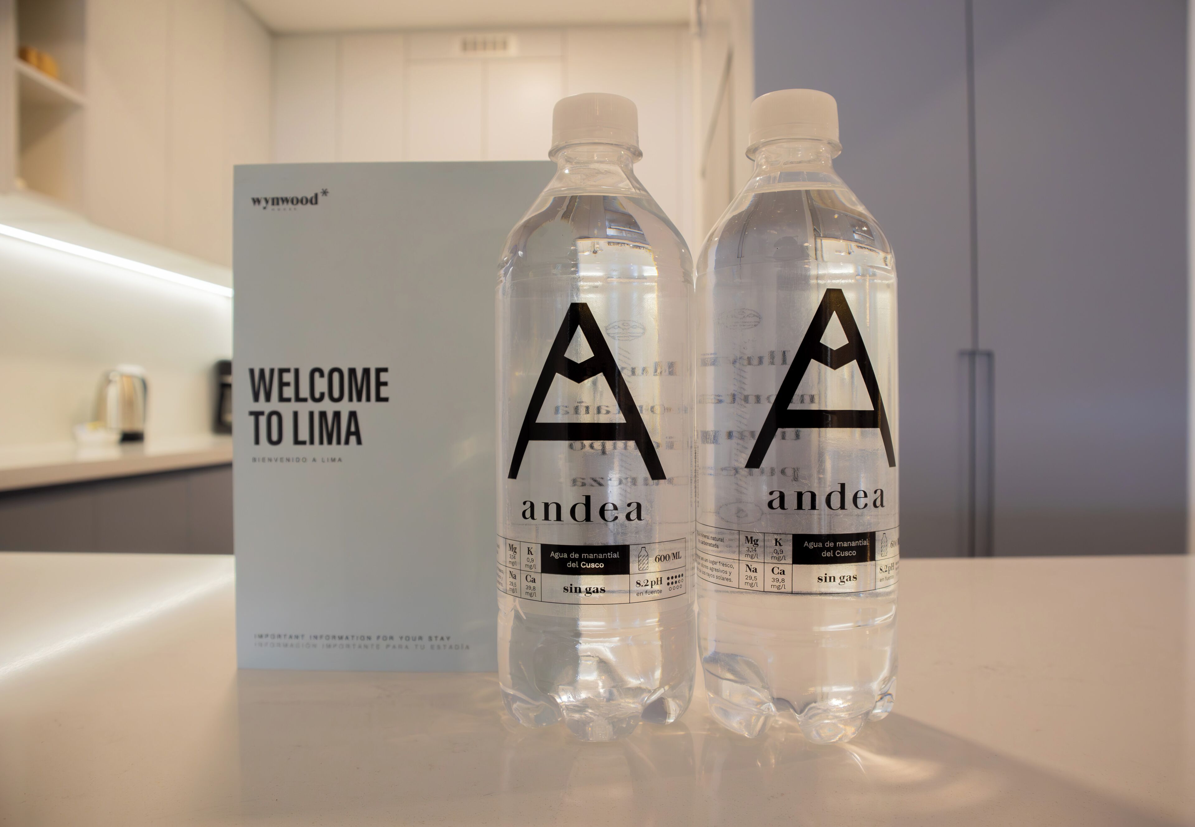 Two water bottles with 'andea' branding on a counter, a 'WELCOME TO LIMA' sign, and a modern interior.