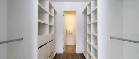 Un couloir étroit aux murs blancs et au plancher en bois, qui mène à une porte sur laquelle est accrochée une serviette.