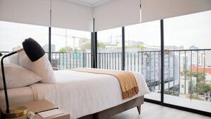 Un dormitorio moderno con una cama grande, una mesita de noche y vistas a la ciudad a través de amplias ventanas.