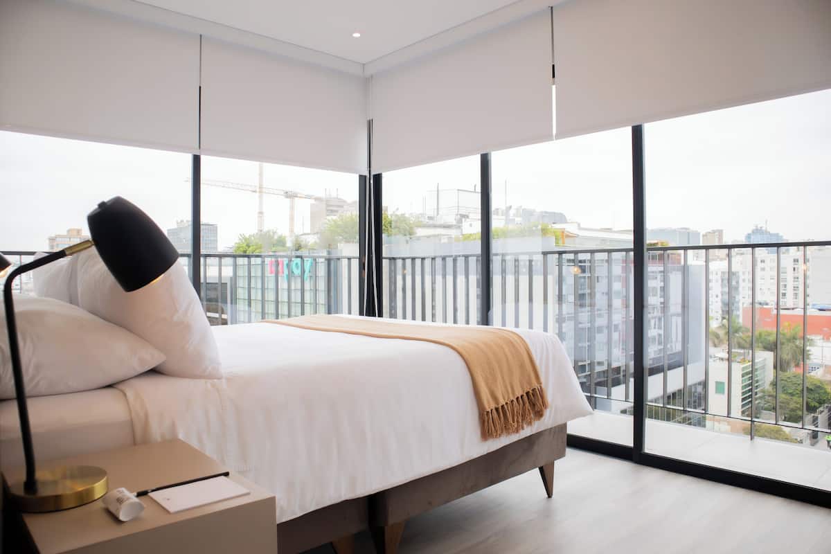 A modern bedroom with a large bed, a bedside table, and a view of the city through large windows.