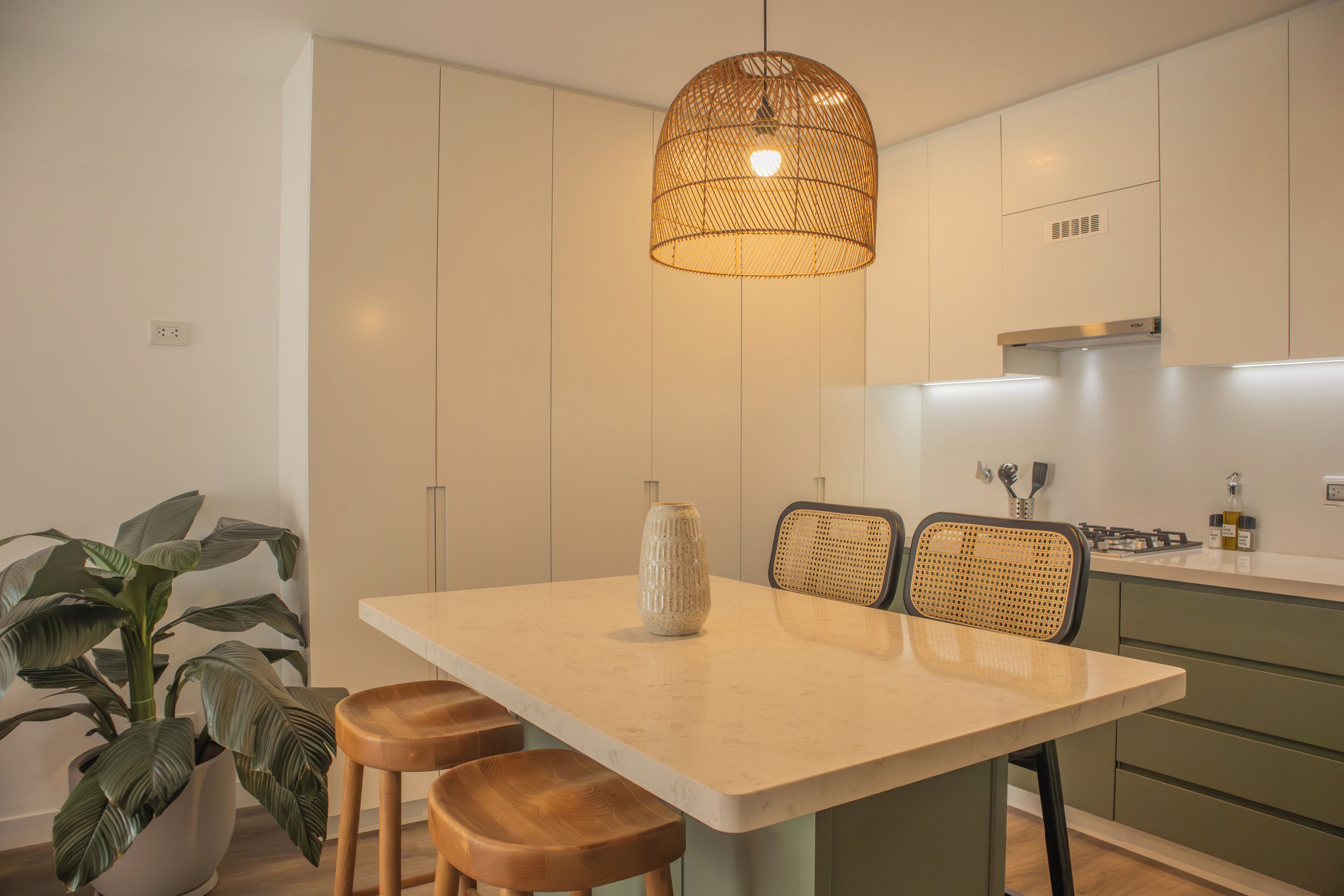 A modern kitchen with a large island, green cabinets, and a hanging light fixture.