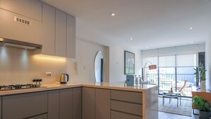 Una cocina moderna con gabinetes grises, estufa integrada y un amplio ventanal con vistas a un balcón.