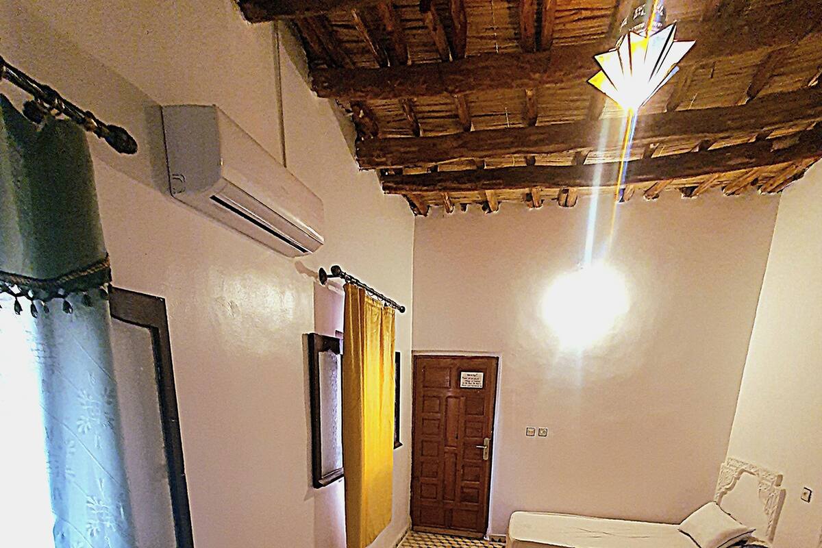 Ein Zimmer mit einem gemusterten Boden, einem Bett mit weißer Bettwäsche, einer Holztür und einer Decke mit freiliegenden Balken.