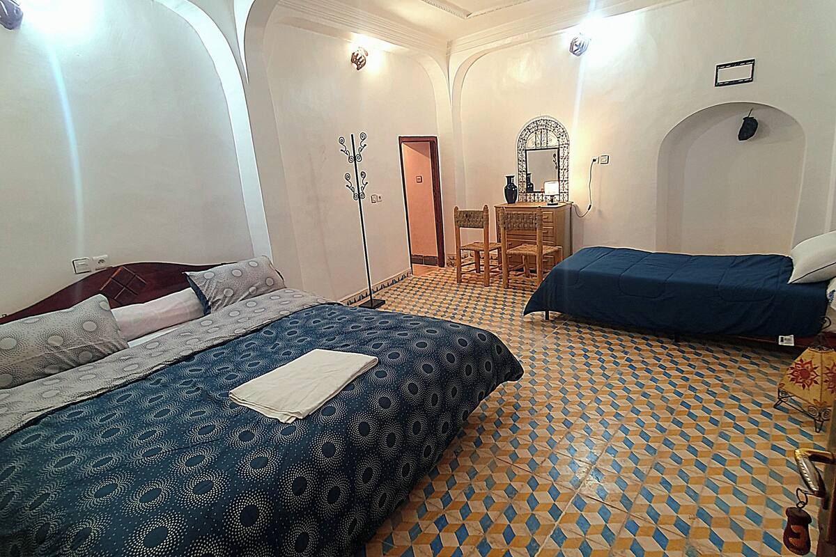 Ein Schlafzimmer mit einem großen Bett, einem Einzelbett, einem Schreibtisch mit Stuhl und einem Spiegel.