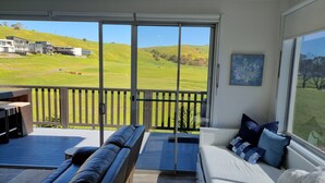 Ein Balkon mit einer Couch und einem Essbereich, mit Blick auf eine grüne Landschaft mit Hügeln und einem Golfplatz.